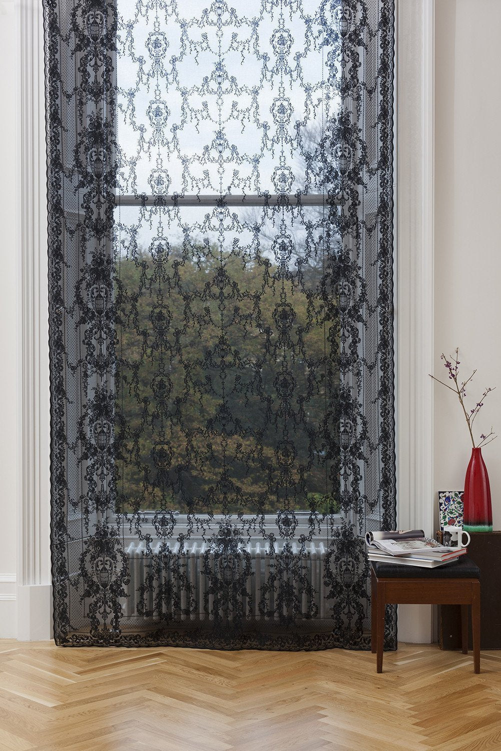 Black sheer cotton lace curtain panel with intricate floral patterns and scalloped edges hanging in a window.
