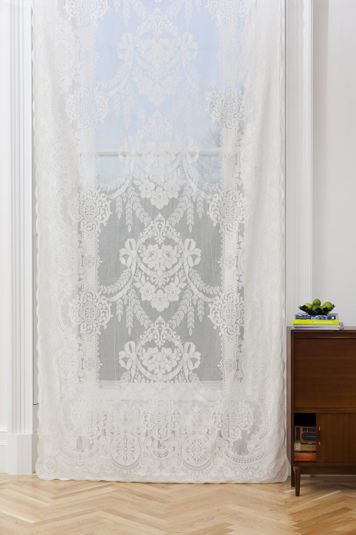 White cotton sheer curtain panel with intricate floral lace patterns, scalloped edges, and a classic rod pocket design.