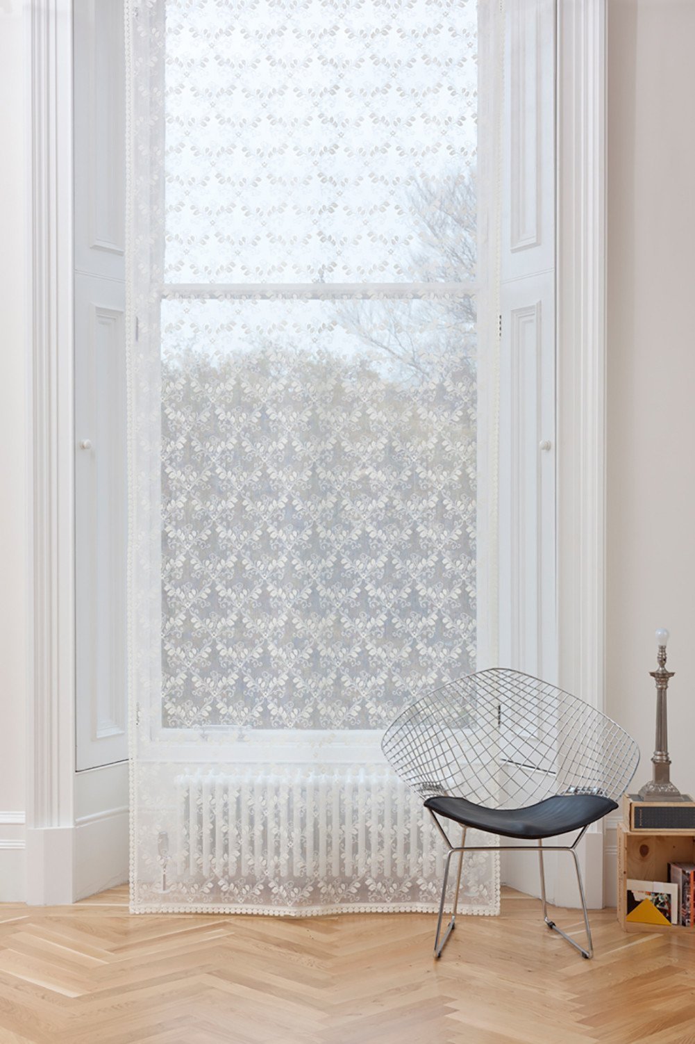 White Scottish lace window panel with a trellis pattern, scalloped edges, and a rod pocket top in a modern room.