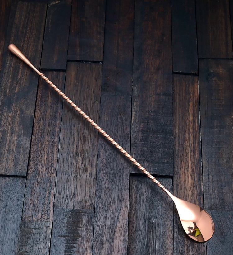 Japanese-style 11.75-inch copper cocktail bar spoon with a twisted handle and weighted teardrop end on dark wood.